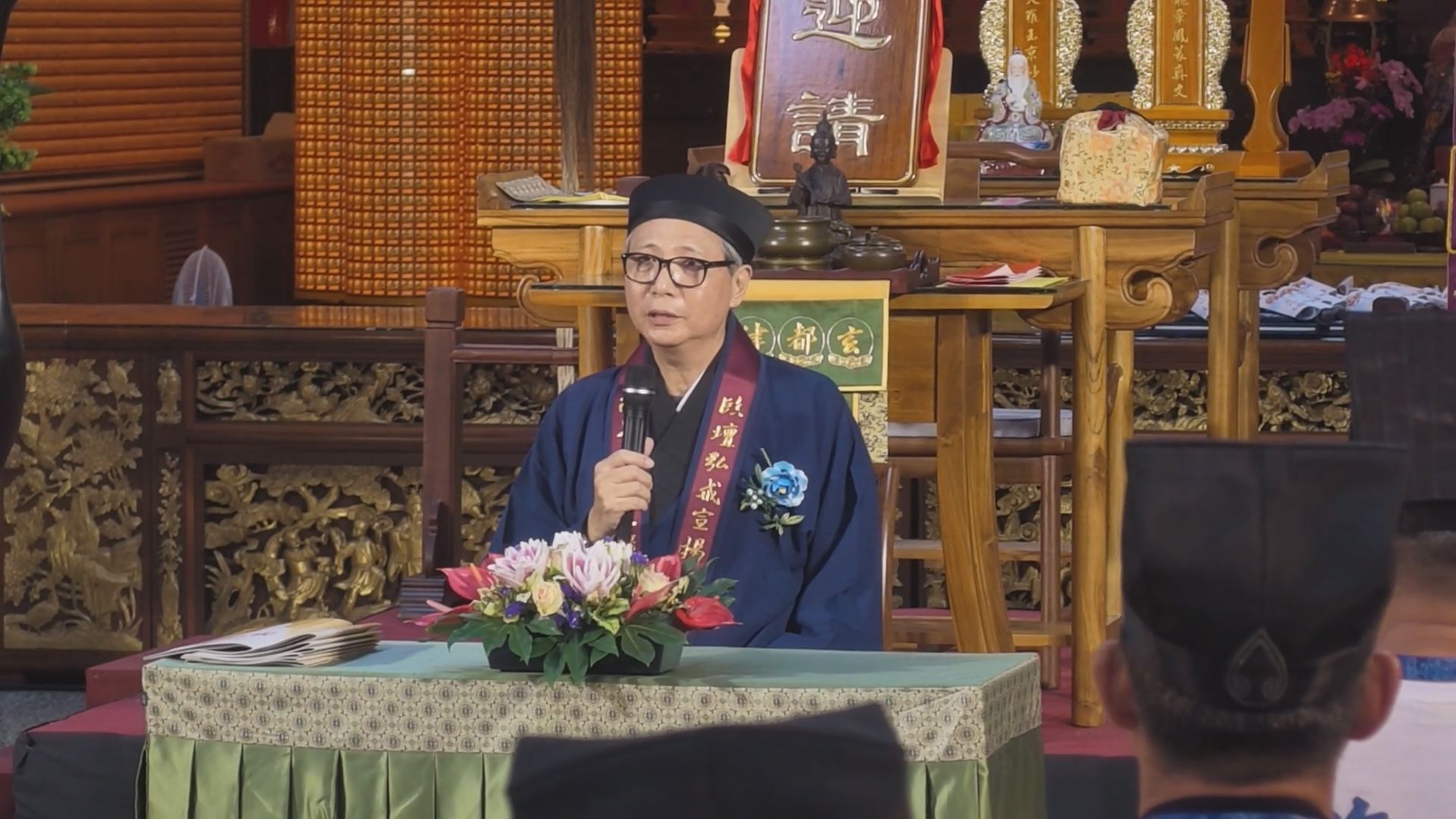 全真龍門派陳理義道長於高雄關帝廟「玄都律壇」前手持麥克風,向現場戒子宣講道教
