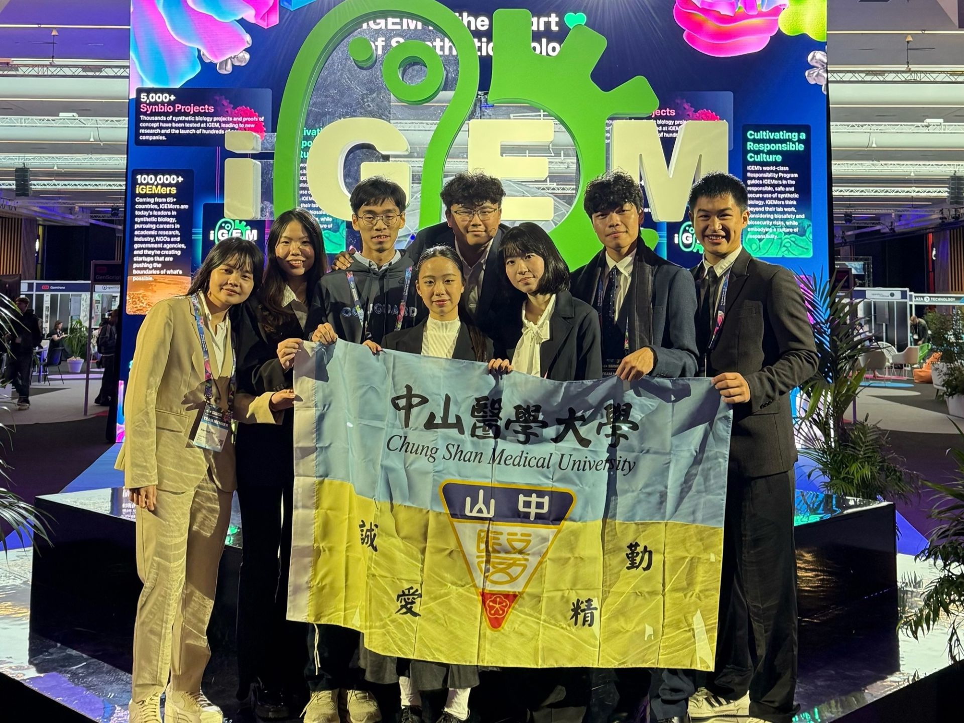 中山醫大 iGEM 團隊在巴黎凡爾賽門展覽中心合影,手持中山醫大旗幟,展現勇奪銀牌後的榮耀時刻。