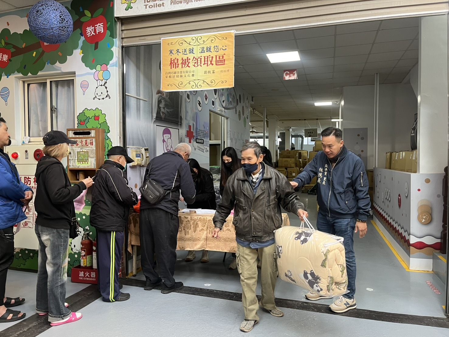 寒冬送暖活動現場，民眾依序排隊領取發熱棉被，工作人員協助登記與發放流程，現場秩序井然。