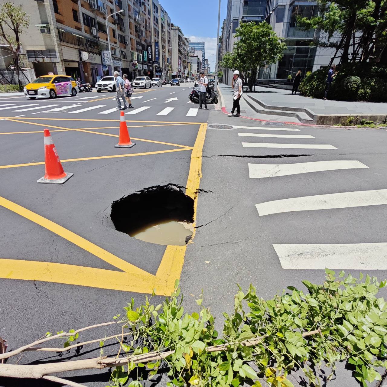 ▲警消人員獲報趕抵，立即於坑洞四周設置三角錐與警示線，封鎖下陷區域，以防止行人與車輛誤入。（翻攝畫面）