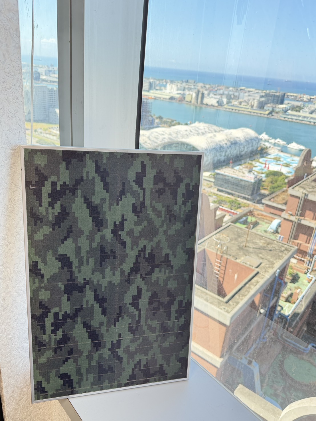 圖說：港灣城市天際線前的迷彩光電示範板，象徵未來建築不僅承載空間功能，更肩負能源與安全角色。睿田能源透過立面彩繪／迷彩光電結合儲能與EMS，將建築升級為可孤島運轉的韌性電力節點，為城市與關鍵設施建立第二道能源防線。